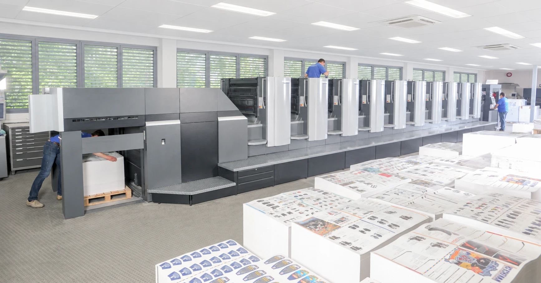Printing press, production team, and stacks of printed materials at LA Print Center’s print shop in Los Angeles